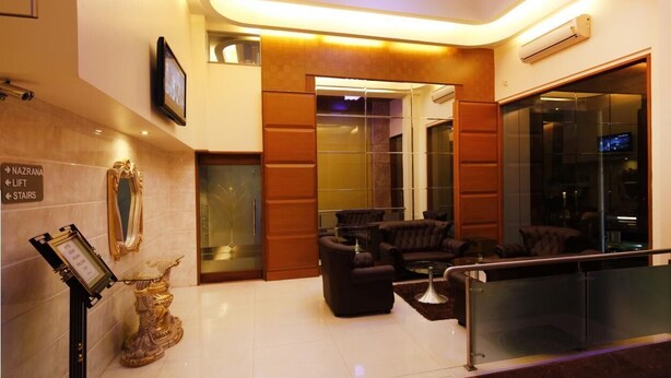 A modern lobby with a reception desk, a seating area, and a glass elevator. - HOTEL SEVEN HEAVEN (Nashik)