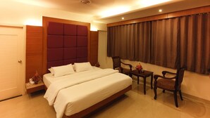 A neatly arranged bedroom with a large bed, a wooden headboard, a small table, and two chairs. - HOTEL SEVEN HEAVEN (Nashik)