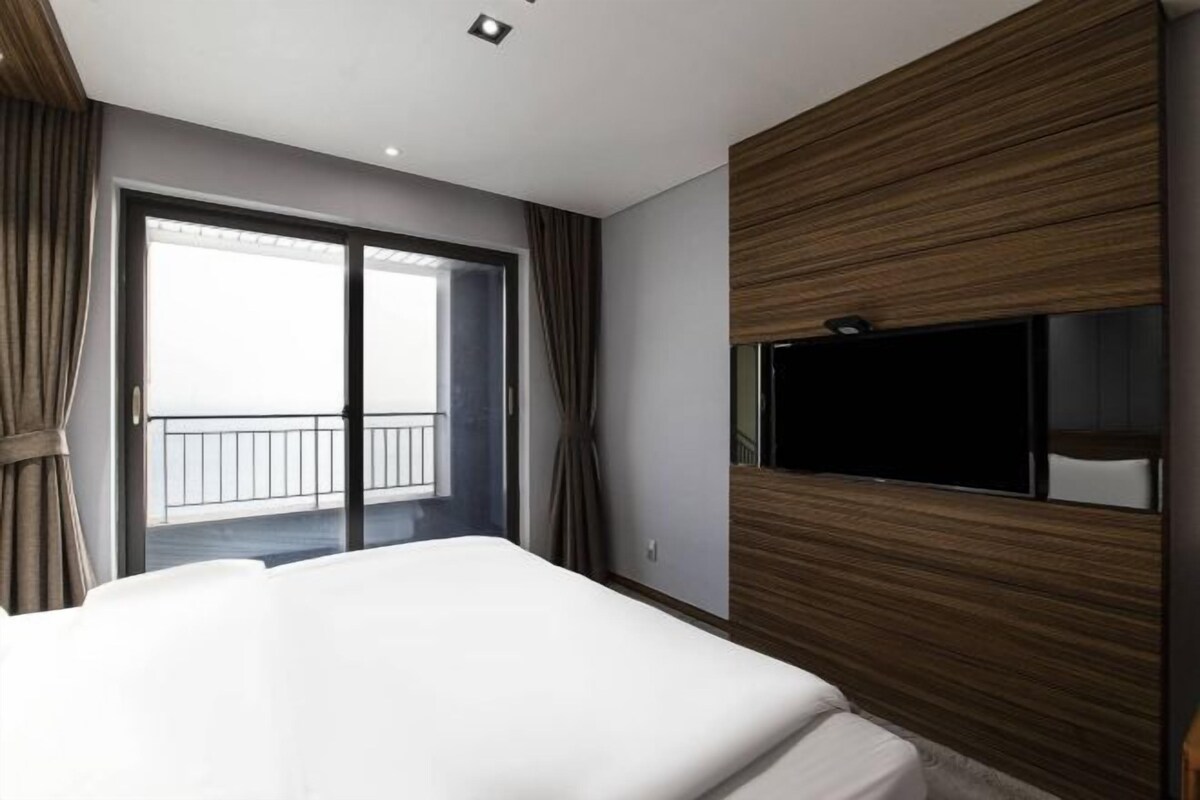 Una habitación de hotel con una cama grande, un televisor montado en la pared y un balcón con cortinas.