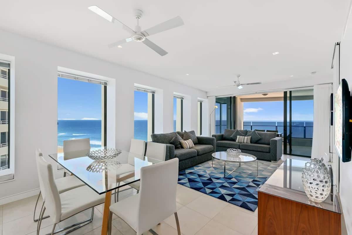 A spacious living area with a large sofa set, a glass dining table, and a view of the ocean.