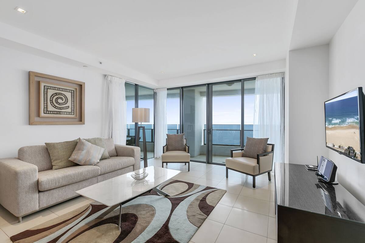 A modern living room with a sofa, armchairs, a coffee table, and a TV.