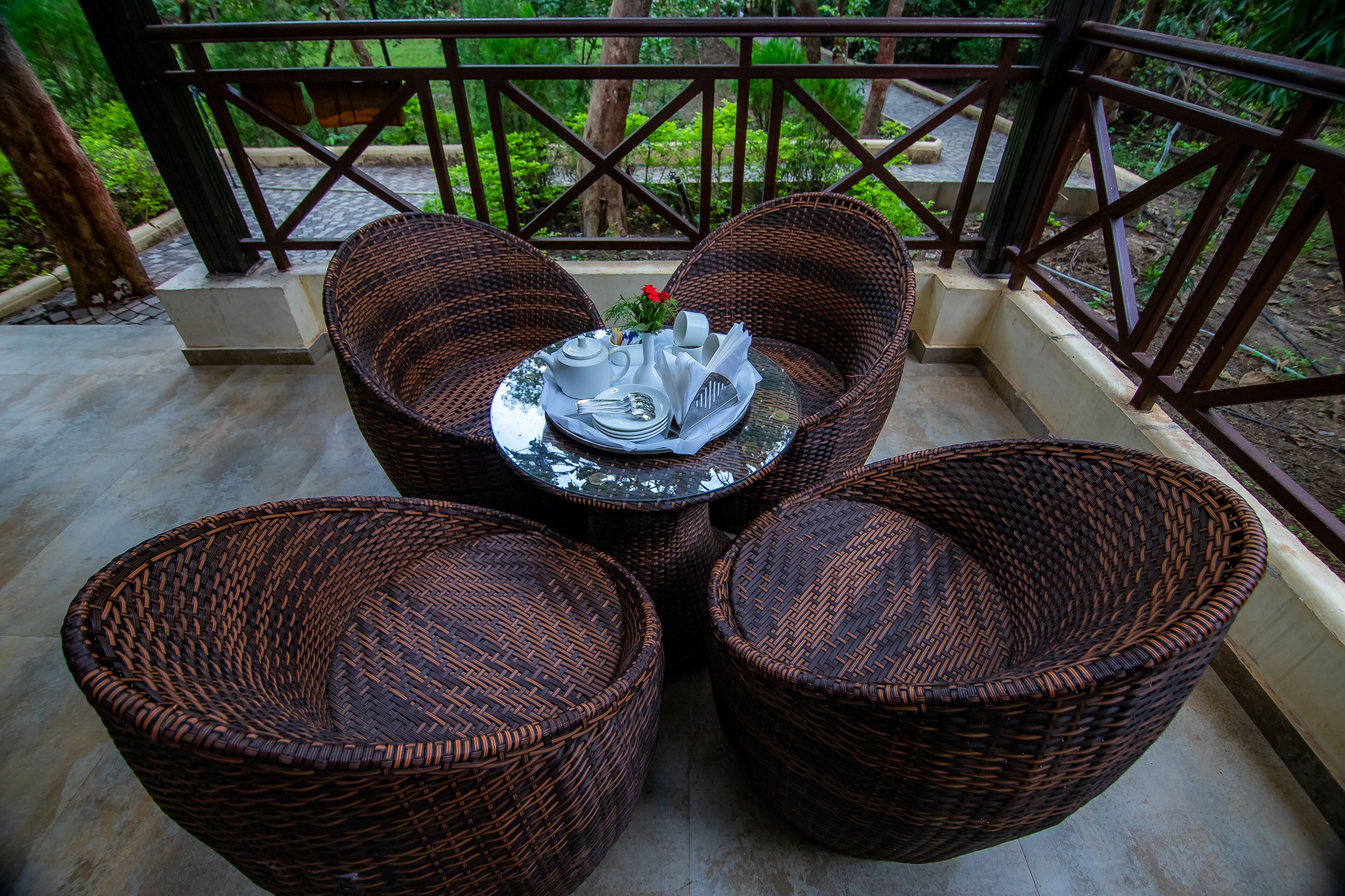 Wicker furniture with a table and chairs on a balcony with a railing.