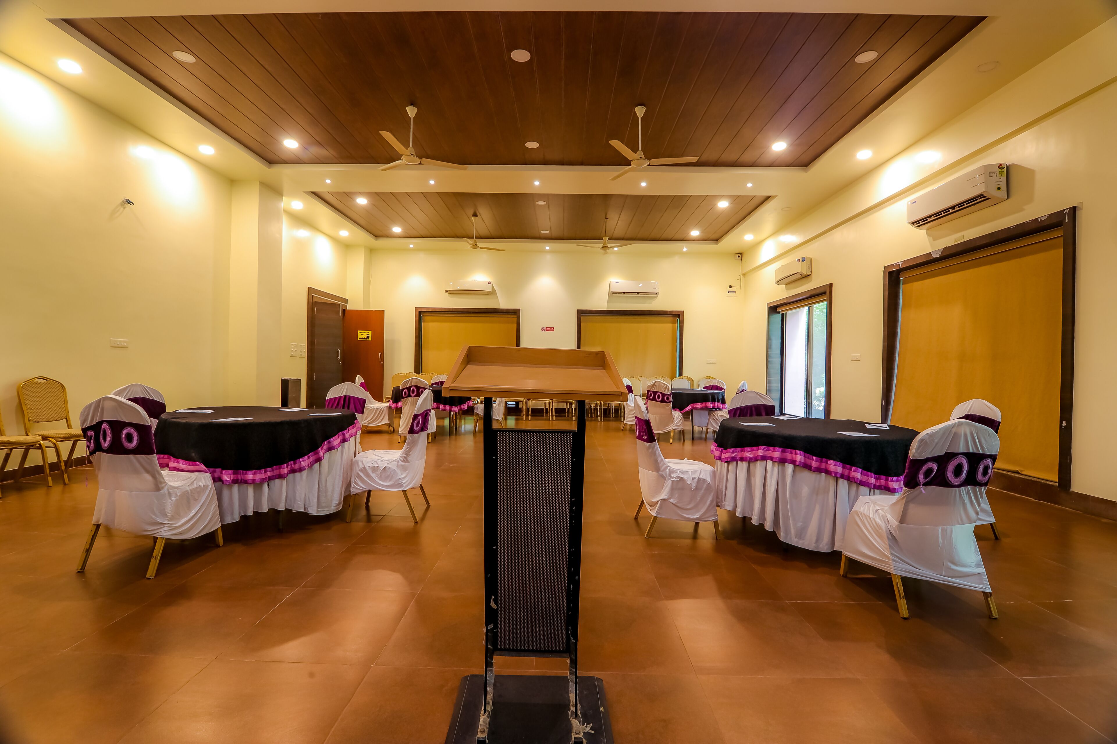 A conference room with a long table, white chairs with pink sashes, wooden ceiling, and ceiling fans.