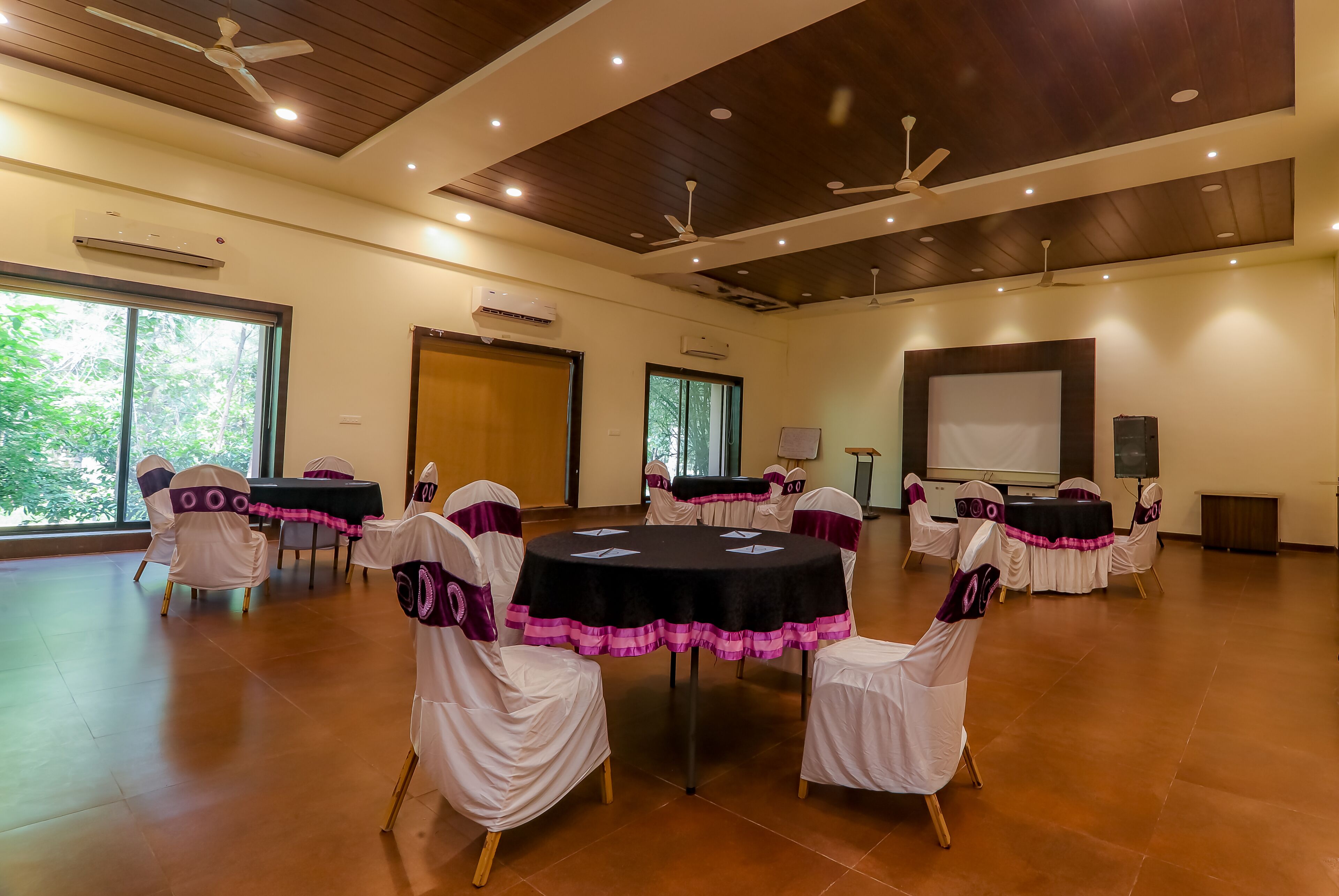 A conference room with round tables, white chairs with purple sashes, and a large screen.