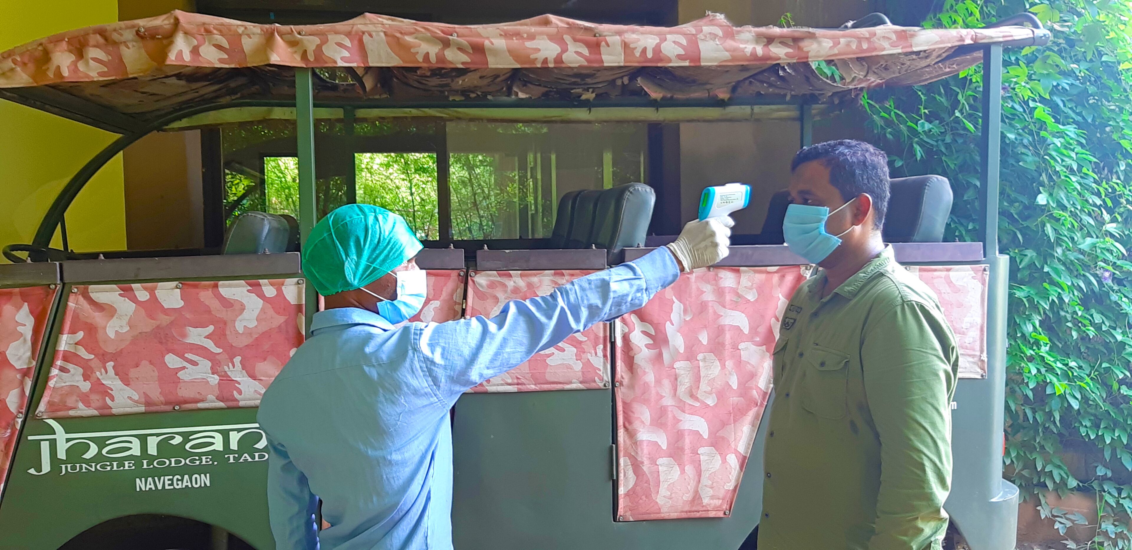 A person wearing a blue shirt and a green head covering, holding a thermometer, and interacting with another person wearing a green shirt.