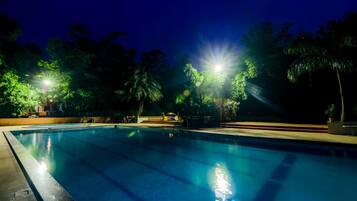 Una piscina nocturna rodeada de árboles y una zona bien iluminada.