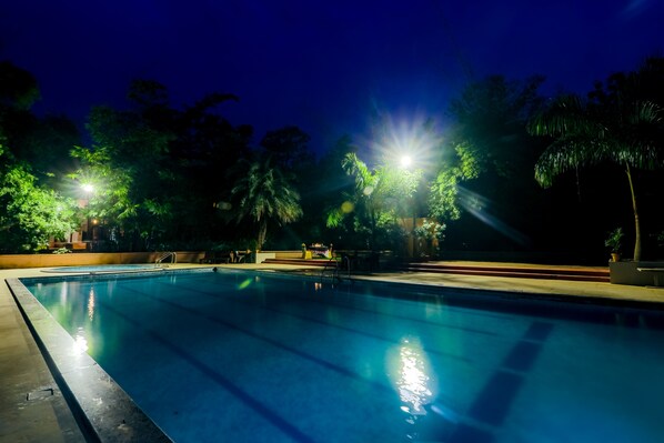 Una piscina nocturna rodeada de árboles y una zona bien iluminada.