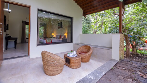 Un espacio de estar al aire libre cubierto con mobiliario de mimbre y una pequeña mesa, con vistas a un exuberante jardín.