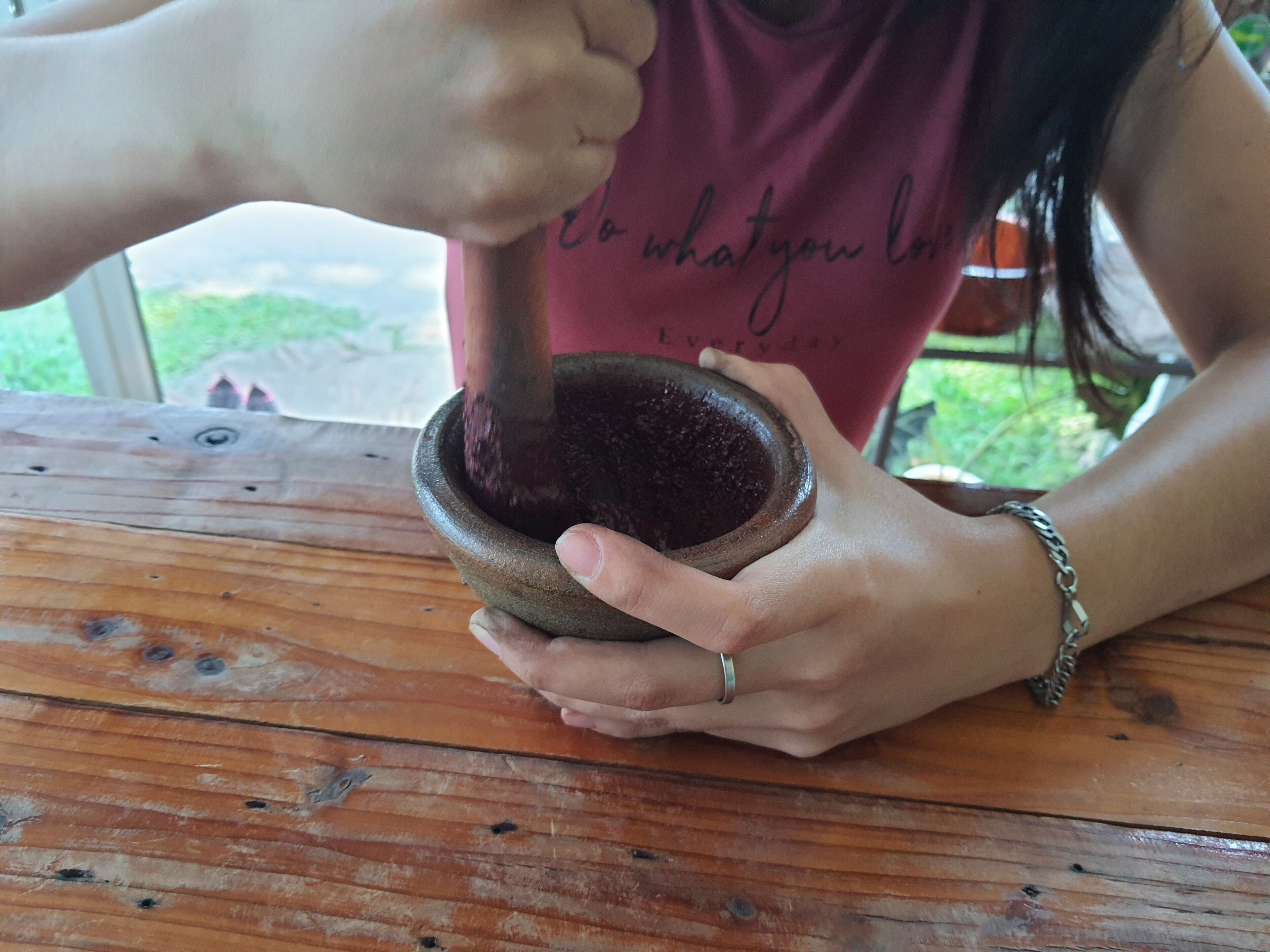 Una persona moliendo ingredientes con un mortero y pilón sobre una mesa de madera.