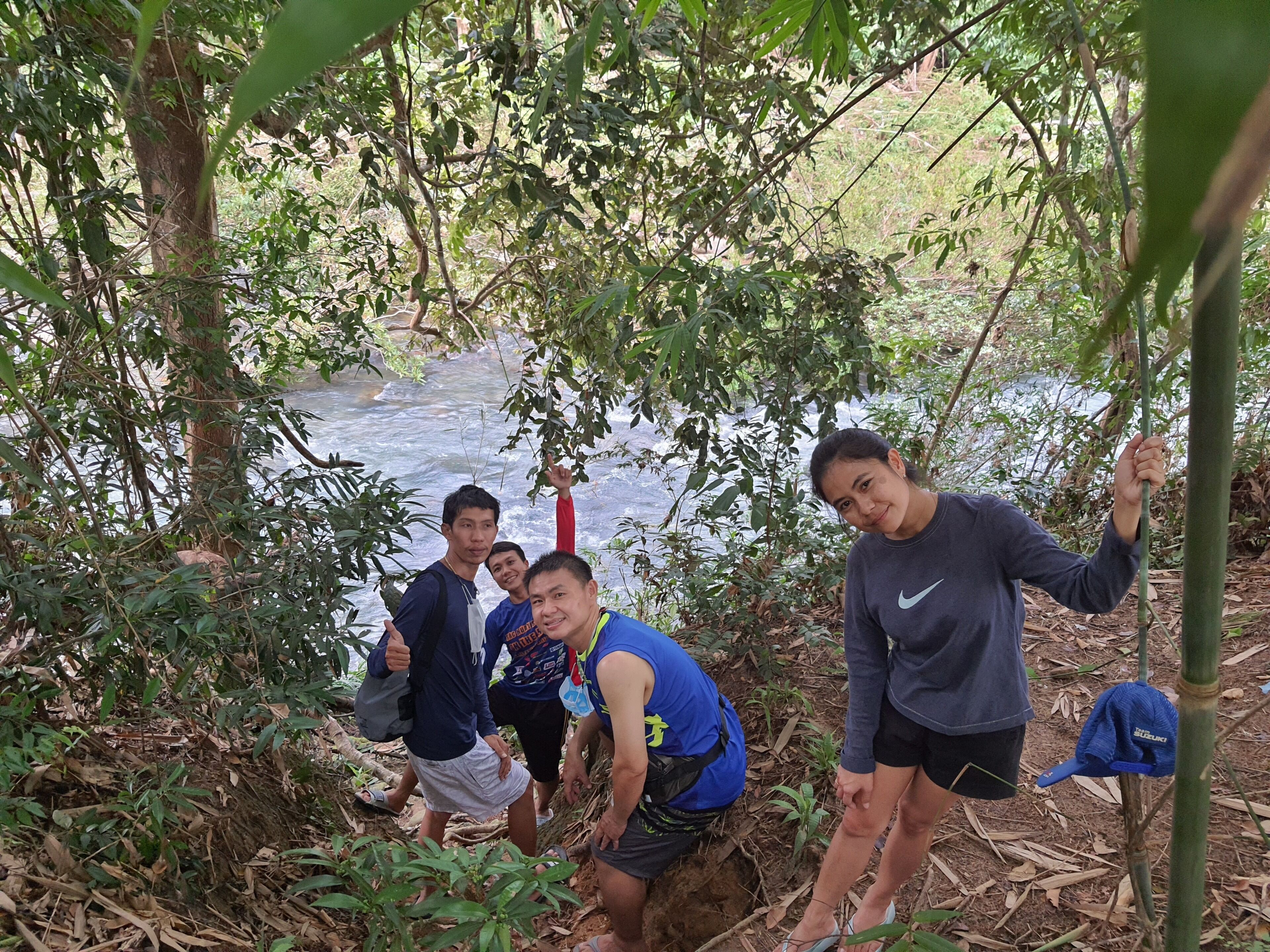 A group of people in a forested area with a stream in the background.