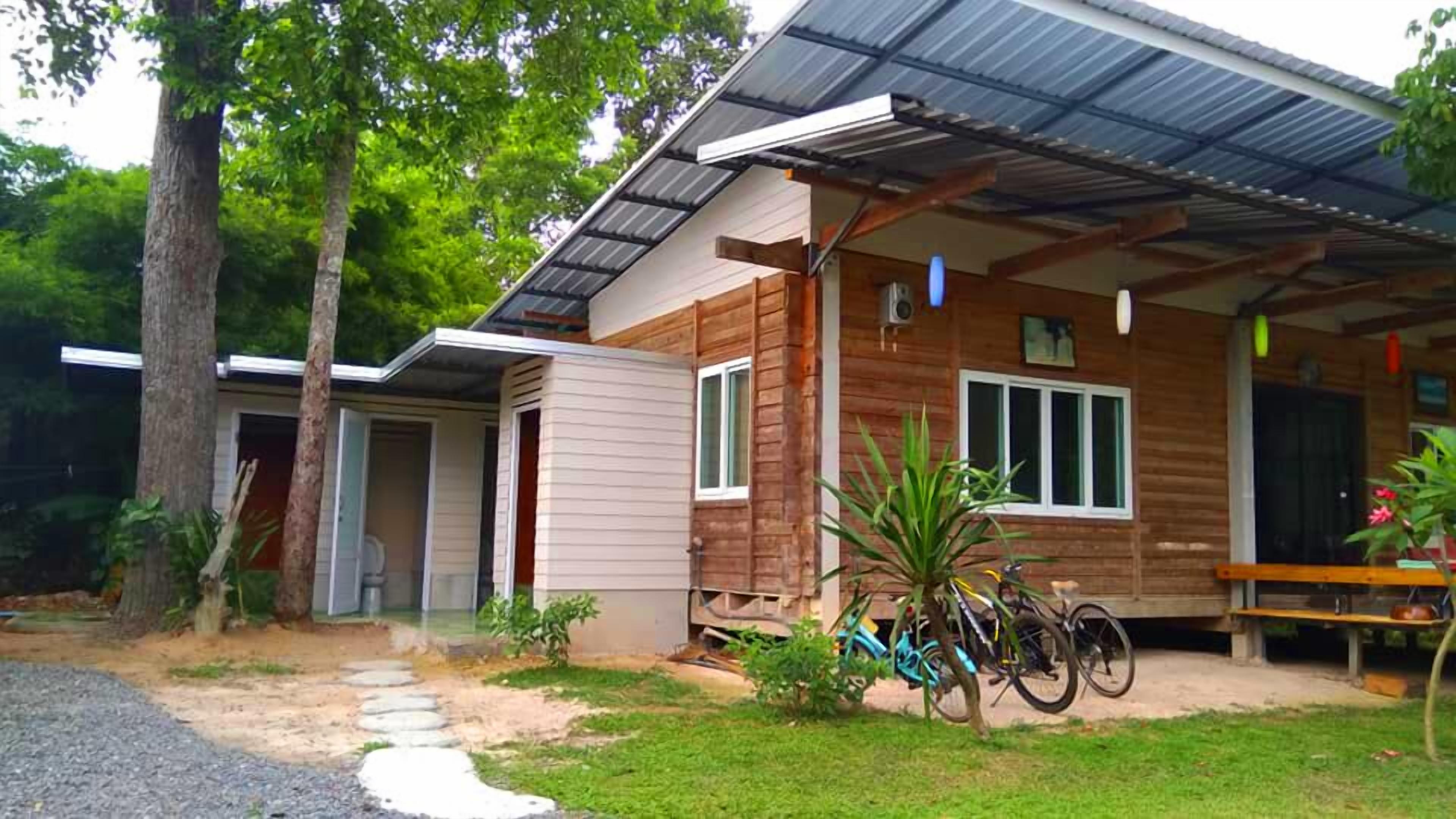 Una casa de madera de dos pisos con un porche cubierto, un pequeño jardín y bicicletas estacionadas afuera.