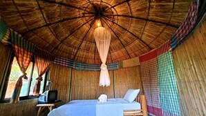 A room with a thatched roof, a bed with a white bedspread, a television on a wooden table, and a window with curtains. - Saengcha Farm Resort (Prachantakham)