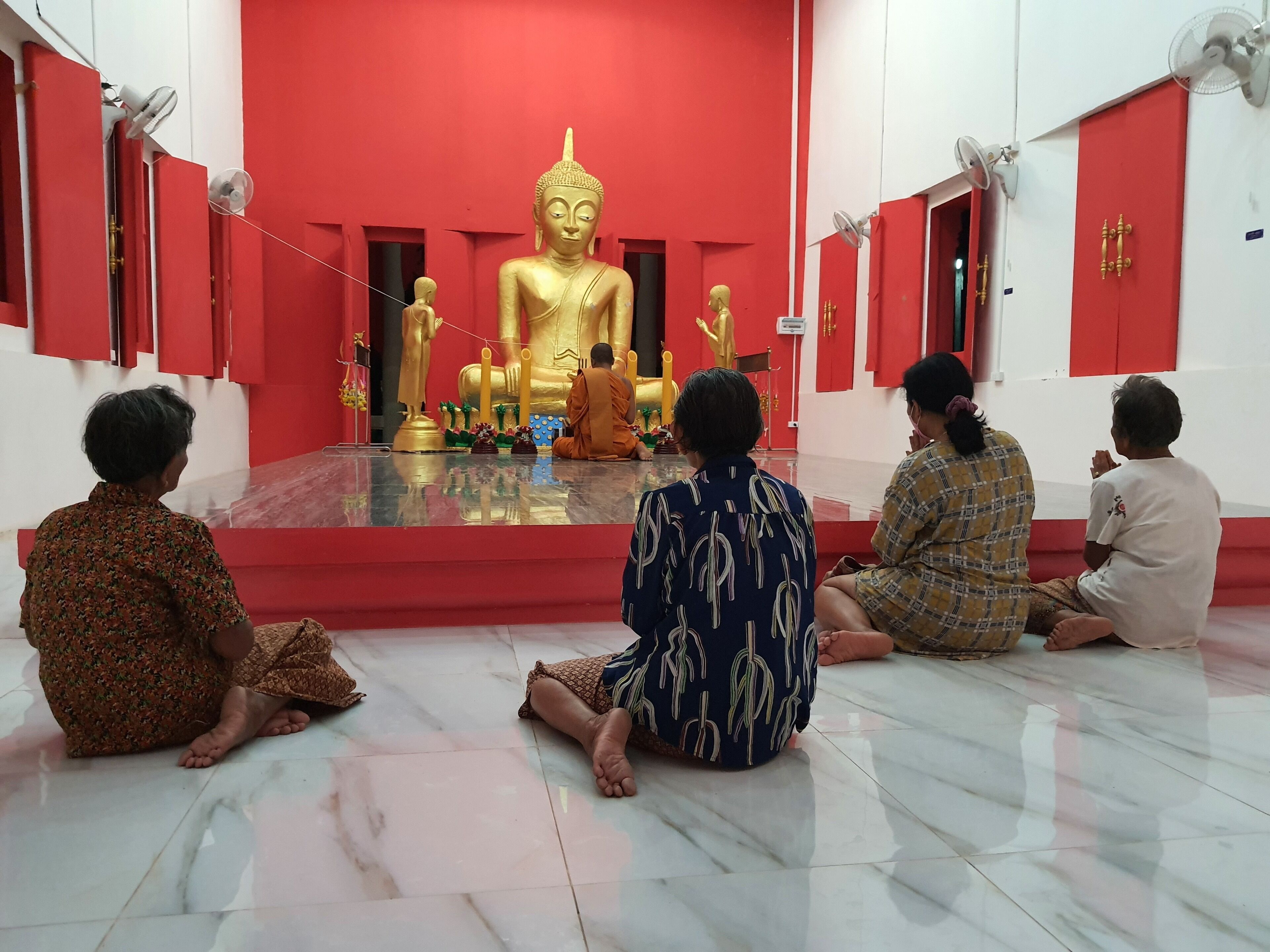 Un grupo de personas sentadas en el suelo de una habitación con una gran estatua dorada en el centro, paredes rojas y techo blanco.