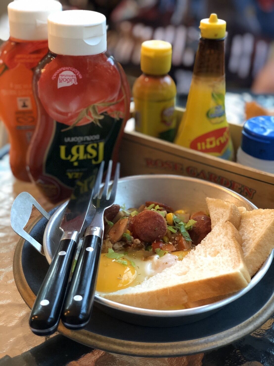 Un plato de comida con pan, salchicha y huevo, acompañado de salsas como kétchup y mostaza.