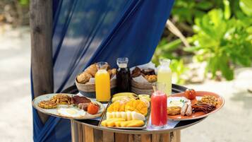 A breakfast spread on a wooden table outdoors with a blue cloth backdrop.