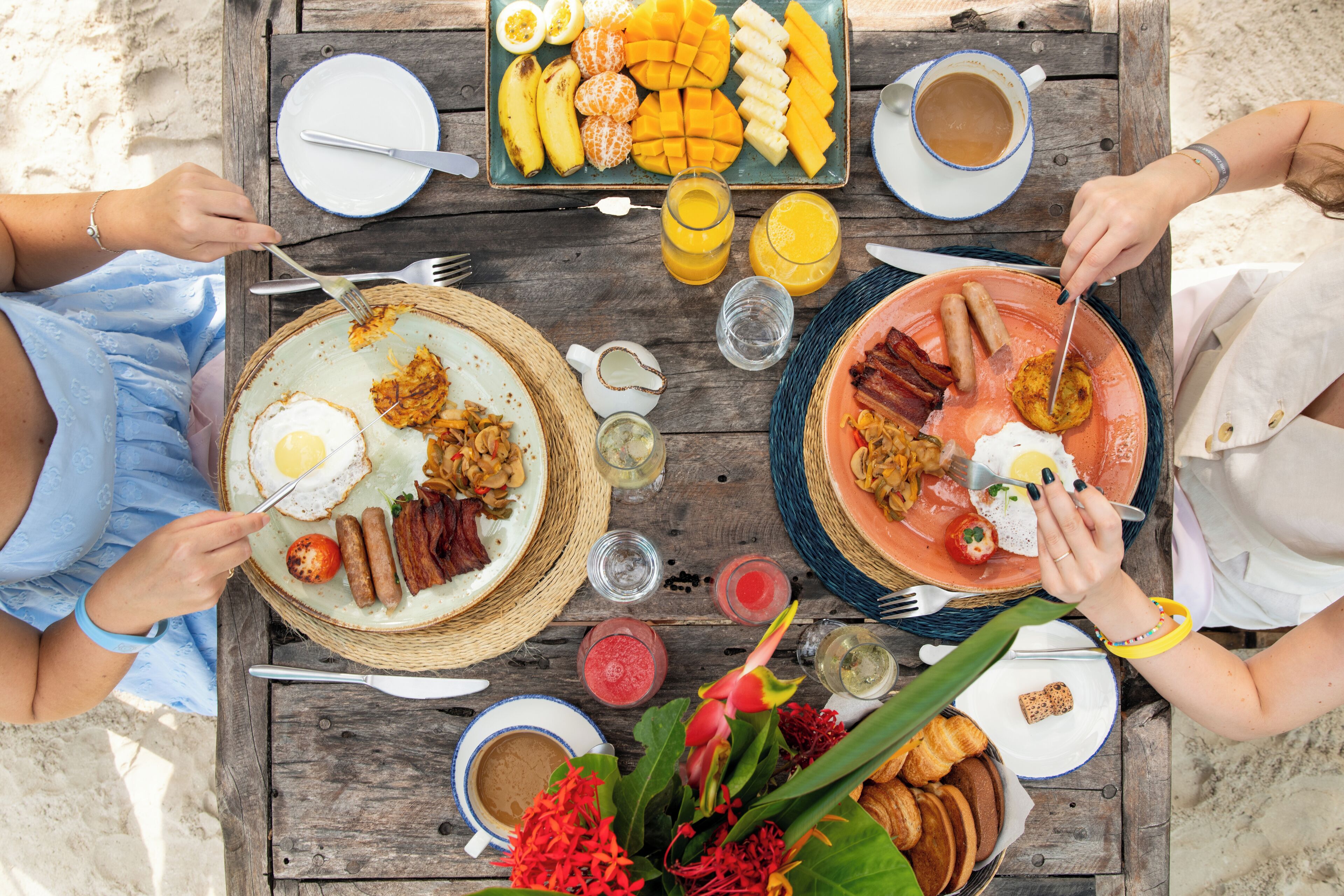Una mesa de madera con artículos para el desayuno, como huevos, salchichas y frutas.