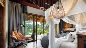 A bedroom with a canopy bed, a hanging chair, and a view of the outdoors.
