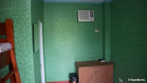 Una habitación con paredes de color verde con estampado, un armario de madera, un cesto de basura negro y una puerta blanca.