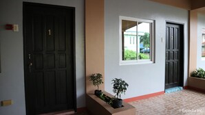 Un pasillo con una puerta de madera oscura marcada con el número 1, un ventanal con vistas a la vegetación y una planta en maceta.