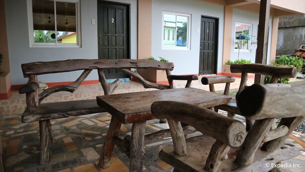 Un espacio al aire libre rústico con bancos y mesas de madera, rodeado de un suelo de baldosas y un muro bajo.
