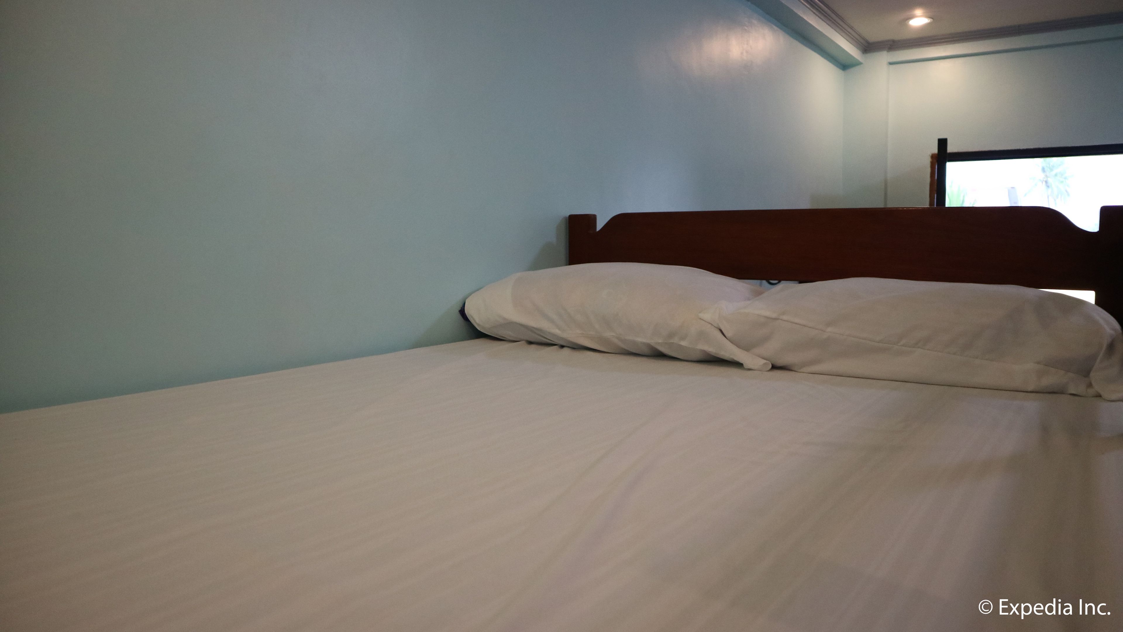 A single bed with white linens in a room with light blue walls and a wooden headboard.