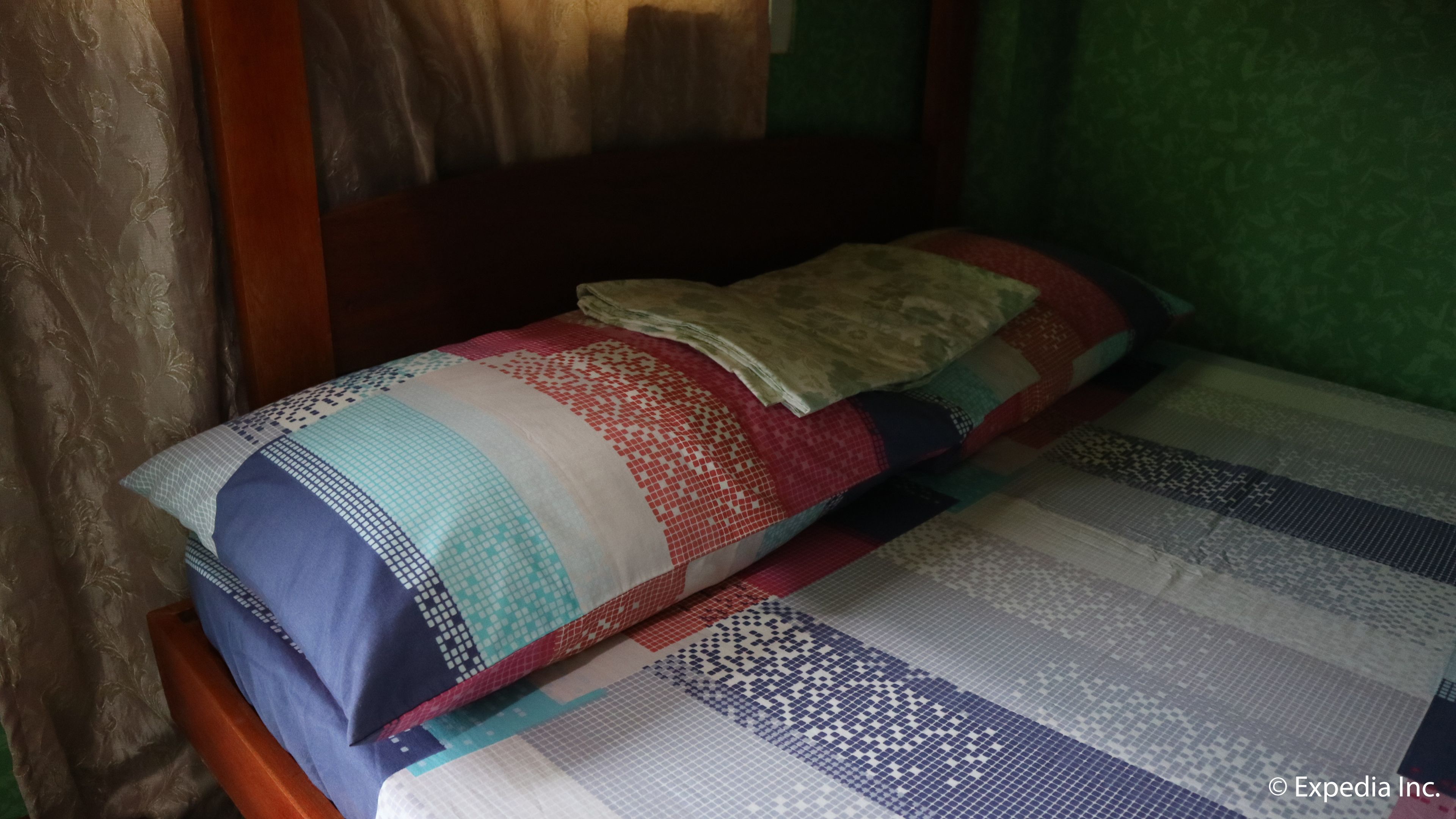 A bed with a quilt and pillows in a room with green walls and a wooden headboard.