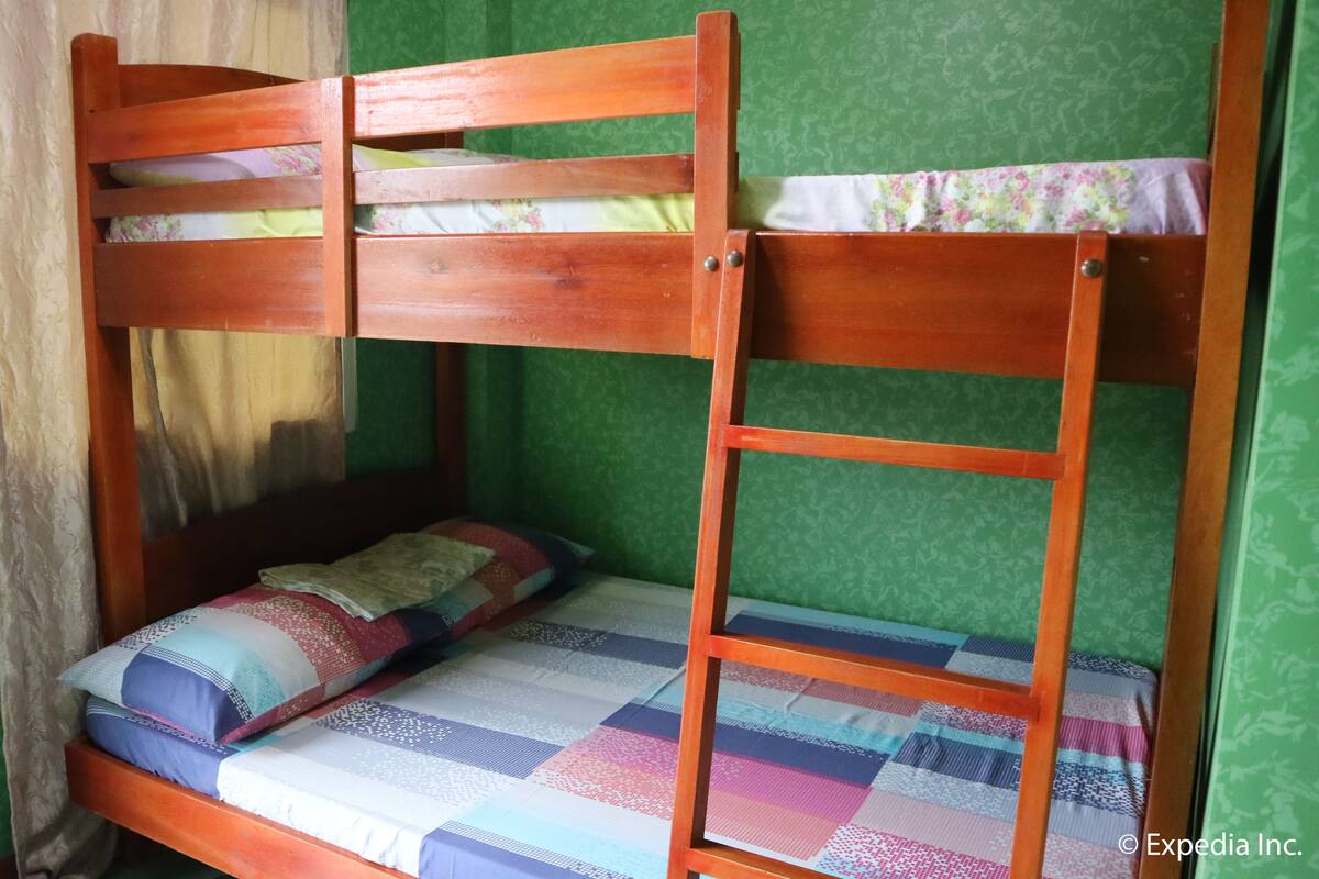 Un lit superposé avec un matelas et des oreillers matelassés, une échelle en bois et une fenêtre avec un rideau.