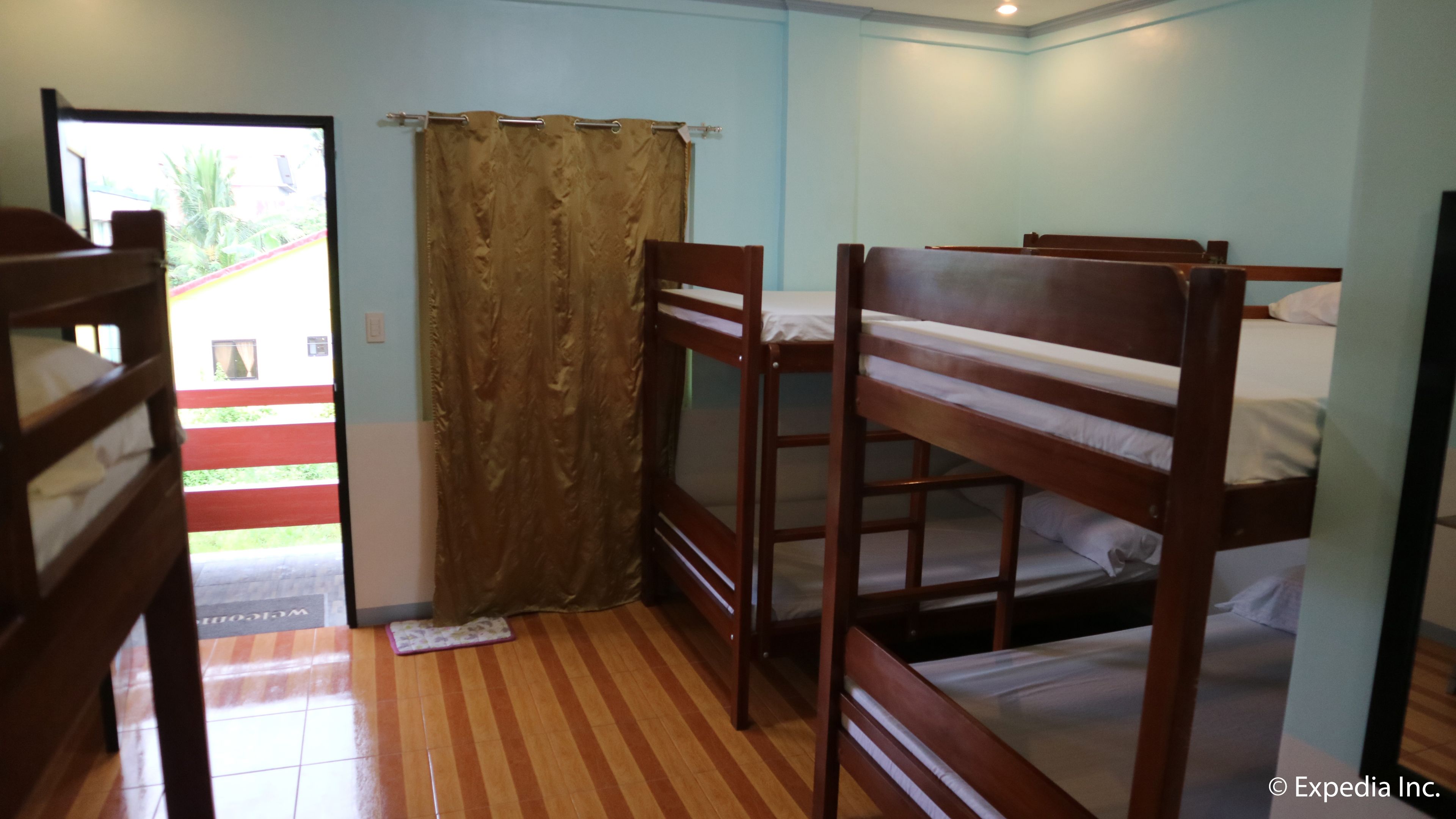 A room with two wooden bunk beds, a curtain, and a door leading to an outdoor area.