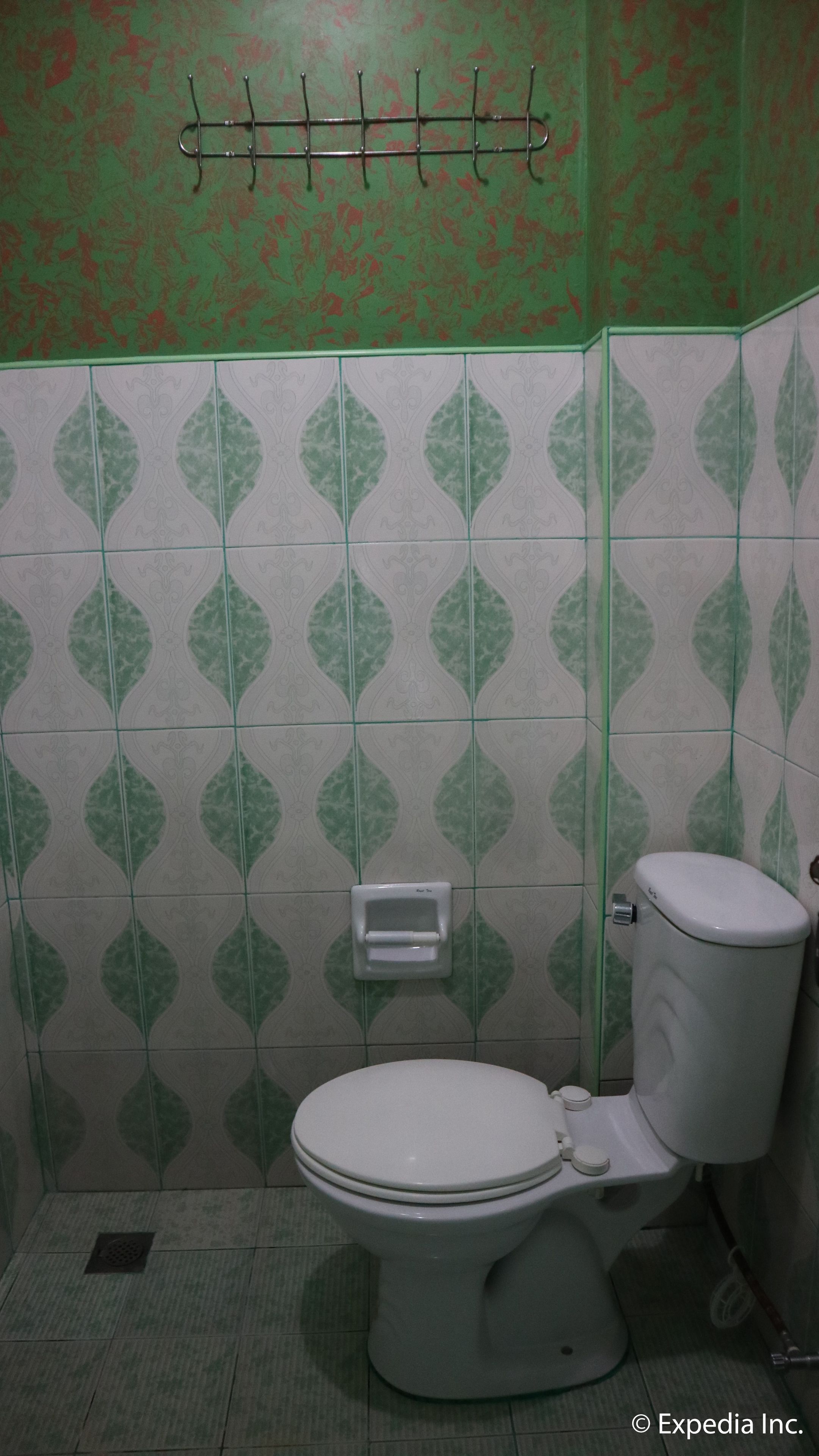 Un baño con un inodoro, un dispensador de toallas de papel y un perchero metálico en la pared.