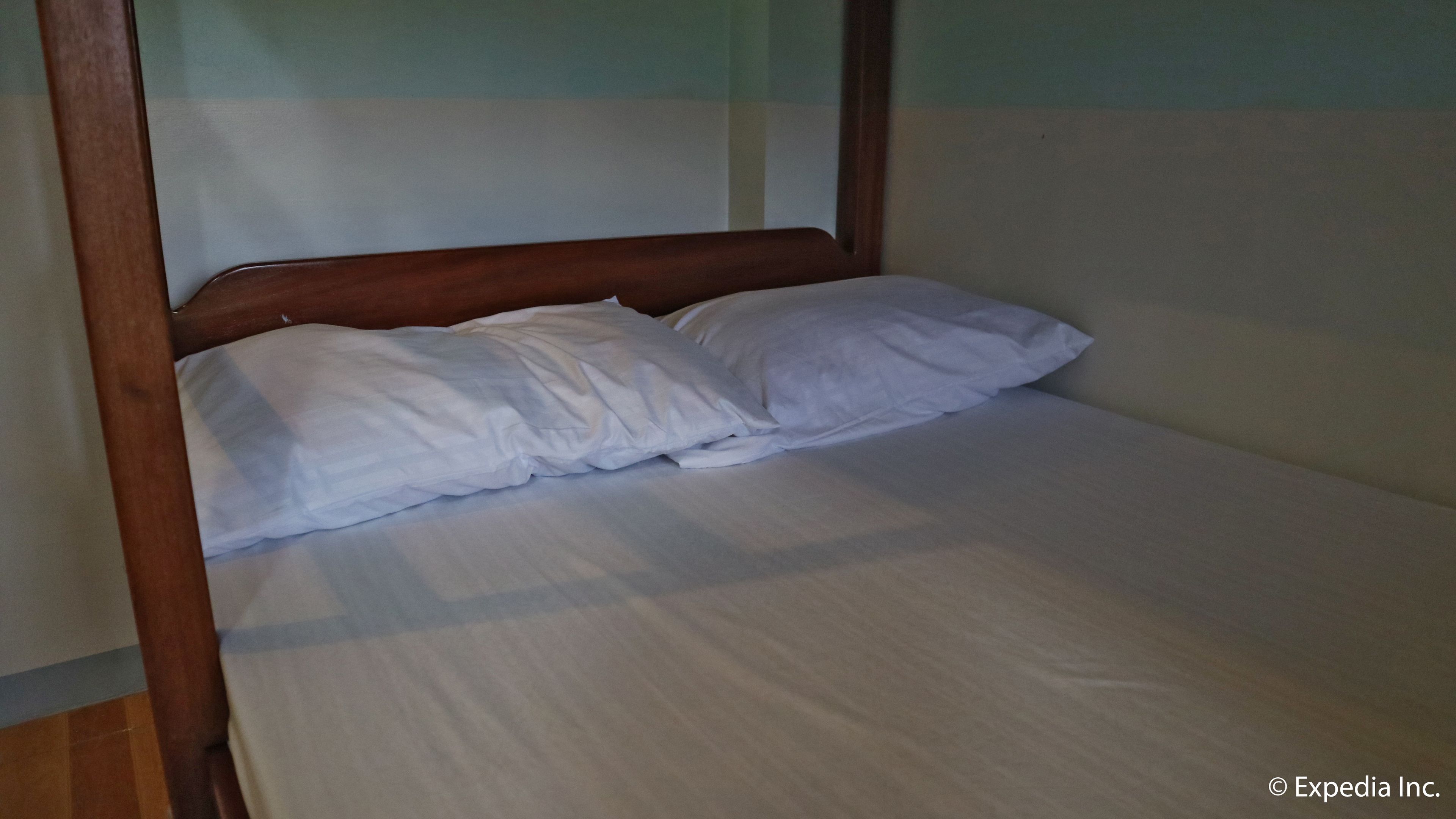 Cama individual con ropa de cama blanca en una habitación con cabecera de madera y paredes de madera.