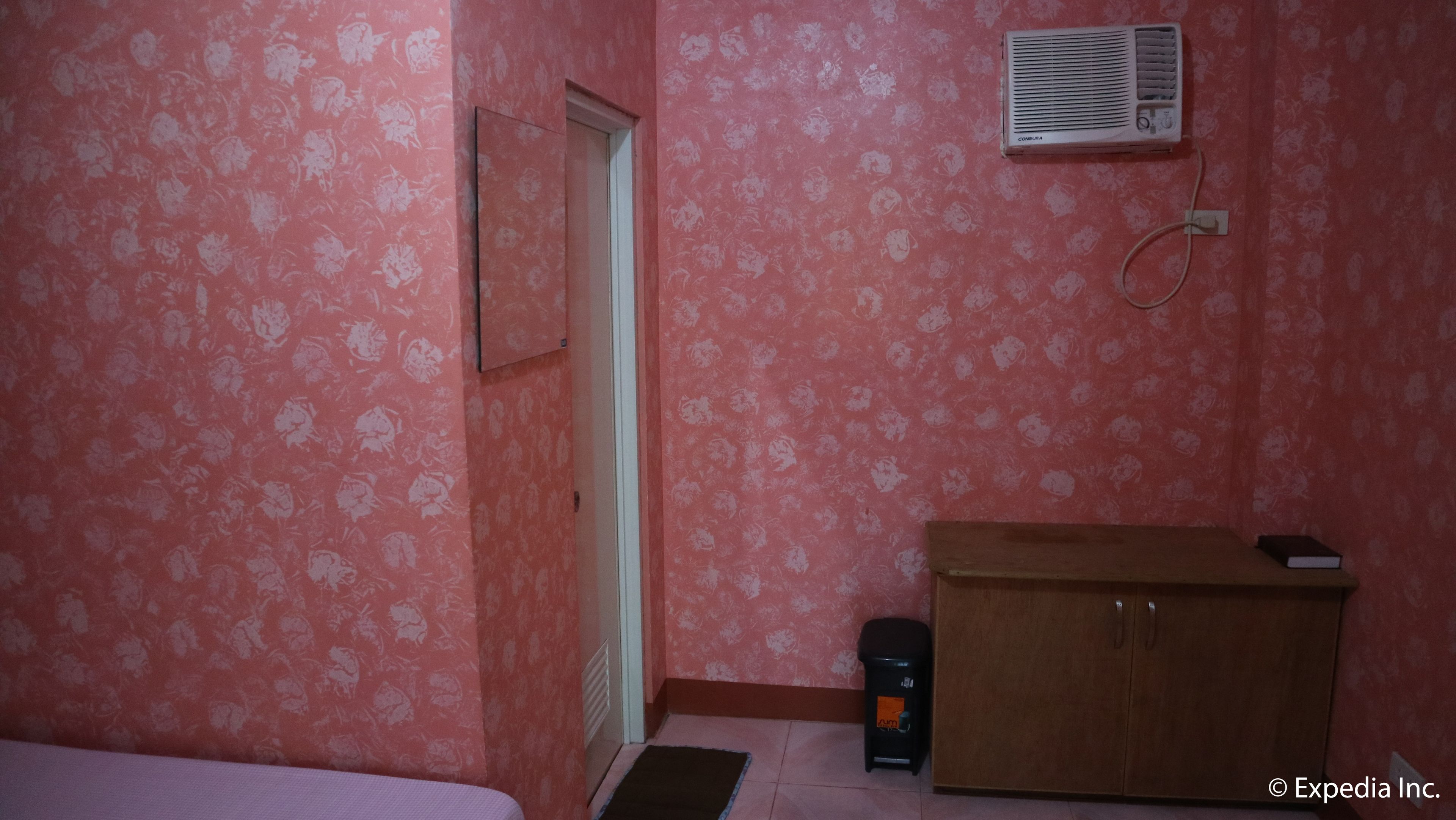 Una habitación con papel tapiz floral rosa, un armario de madera, un pequeño calentador y una puerta.