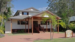 A two-story house with a covered porch, a staircase, and a small garden area with palm trees. - Away on Shirley Lane (Byron Bay)