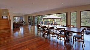 A spacious dining area with a wooden table and chairs, large windows, and a view of the outdoors. - Away on Shirley Lane (Byron Bay)