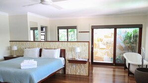 A hotel room with a large bed, two bedside tables with lamps, a bathtub, and a sliding glass door leading to an outdoor area. - Away on Shirley Lane (Byron Bay)