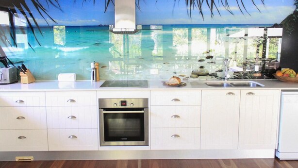 A kitchen with a large island, a Bosch oven, and a view of the ocean through a glass wall. - Away on Shirley Lane (Byron Bay)