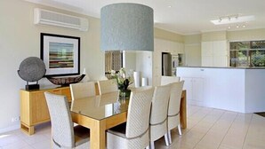 A modern kitchen with white cabinets, a central island, and a dining area with a glass table and chairs. - Away on Massinger Street (Byron Bay)