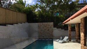 A swimming pool with a tiled deck, surrounded by a stone wall and a wooden fence. - Away on Massinger Street (Byron Bay)
