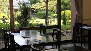 A dining area with a view of a traditional Japanese garden, including a building with a tiled roof. - Beppu Housensou (Beppu)