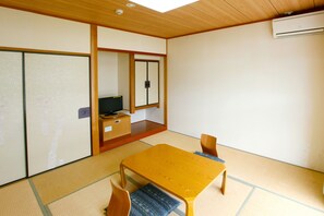 A traditional Japanese room with tatami flooring, a low wooden table, and a television on a cabinet.