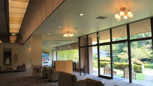 A spacious lobby with seating areas, large windows offering a view of the outdoors, and a reception desk. - Beppu Housensou (Beppu)