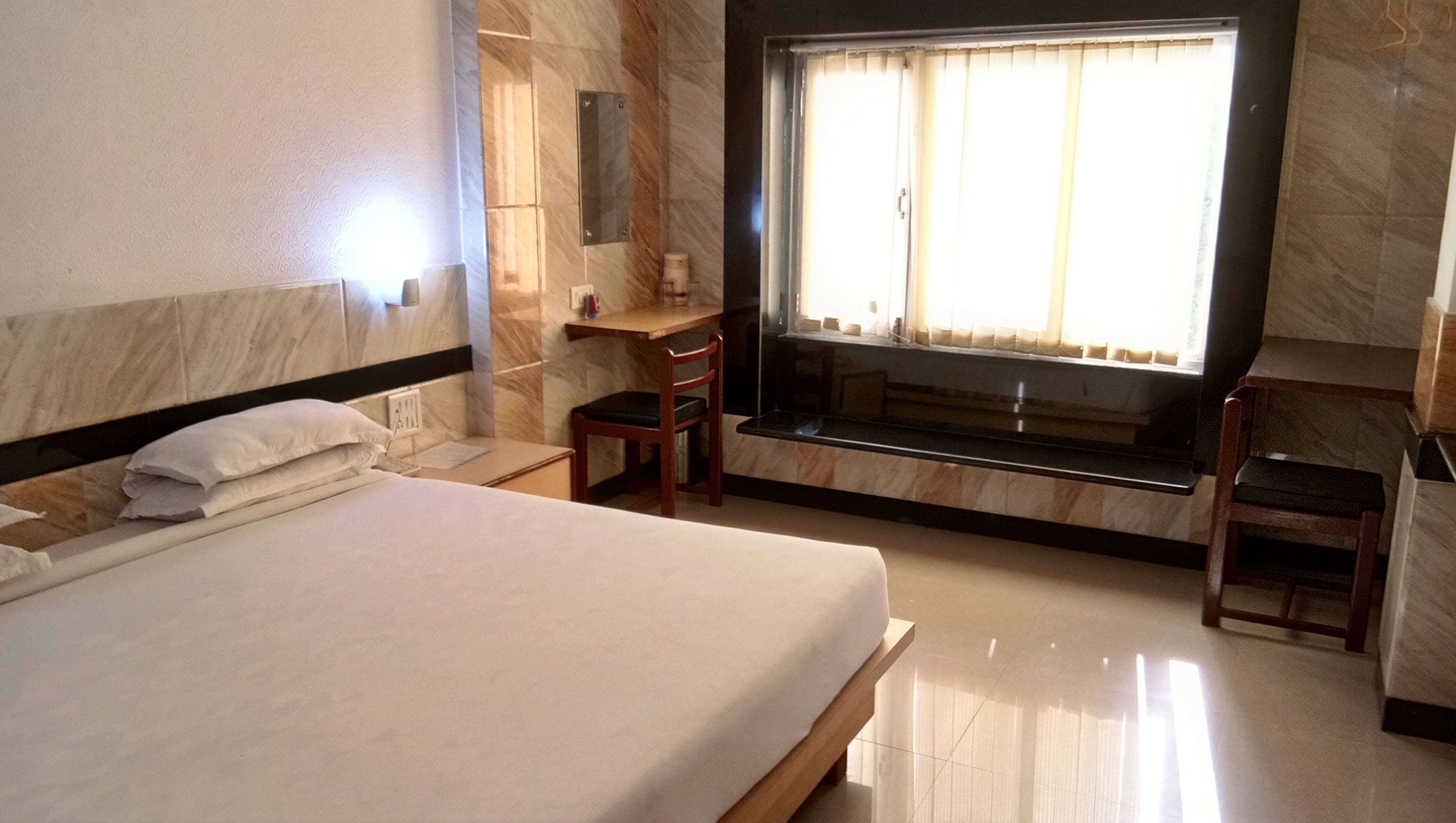 A hotel room with a large bed, a desk, a chair, and a window with curtains.