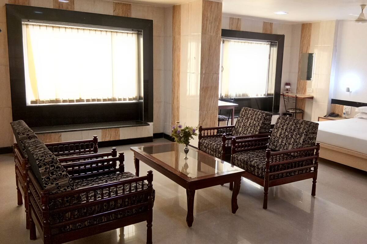 A hotel room with a bed, a TV, a table with chairs, and a window with blinds.
