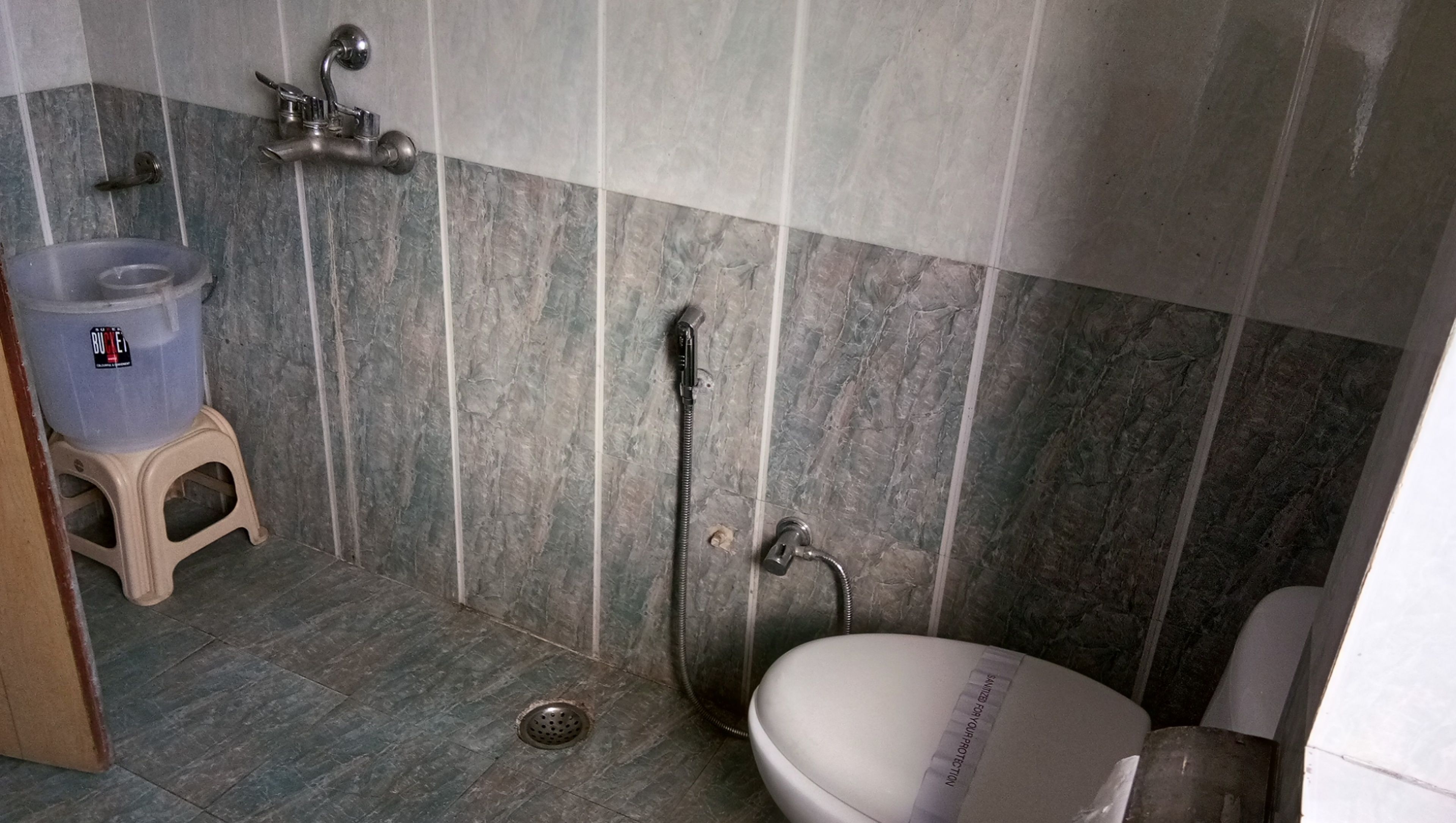 A bathroom with a shower, toilet, and a water dispenser on a stool.