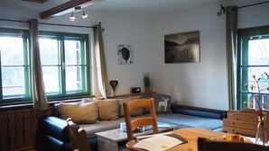 A cozy living room with a wooden dining table, a sofa, and a large window with curtains. - Bei Herrmanns (Sautens)