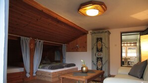 A cozy room with a wooden ceiling, a bed with blue curtains, a small table with a vase, and a sofa with a decorative pillow. - Bei Herrmanns (Sautens)