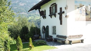 A traditional chalet with a stone bench, a wooden door, and a view of a forested valley. - Bei Herrmanns (Sautens)