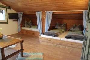 Ein gemütliches Schlafzimmer im Dachgeschoss mit zwei Betten, Holzdielen und einem Fernseher an der Wand.