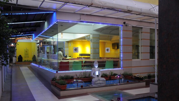 A modern indoor pool area with a Buddha statue, potted plants, and a glass enclosure with a view of the adjacent room. - Maple Suites (Bengaluru)