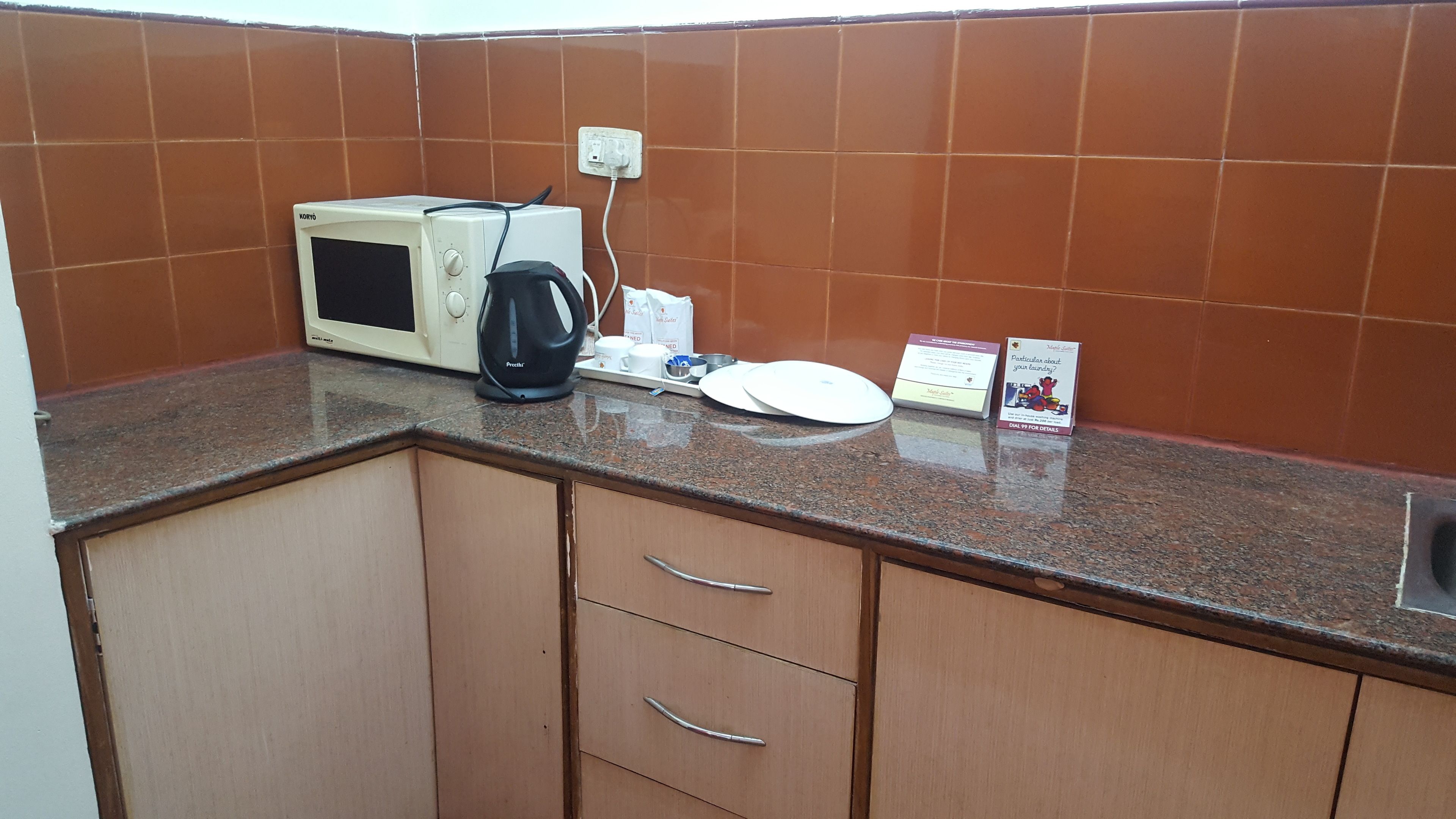 Una cocina con microondas, hervidor y algunos platos sobre la encimera.