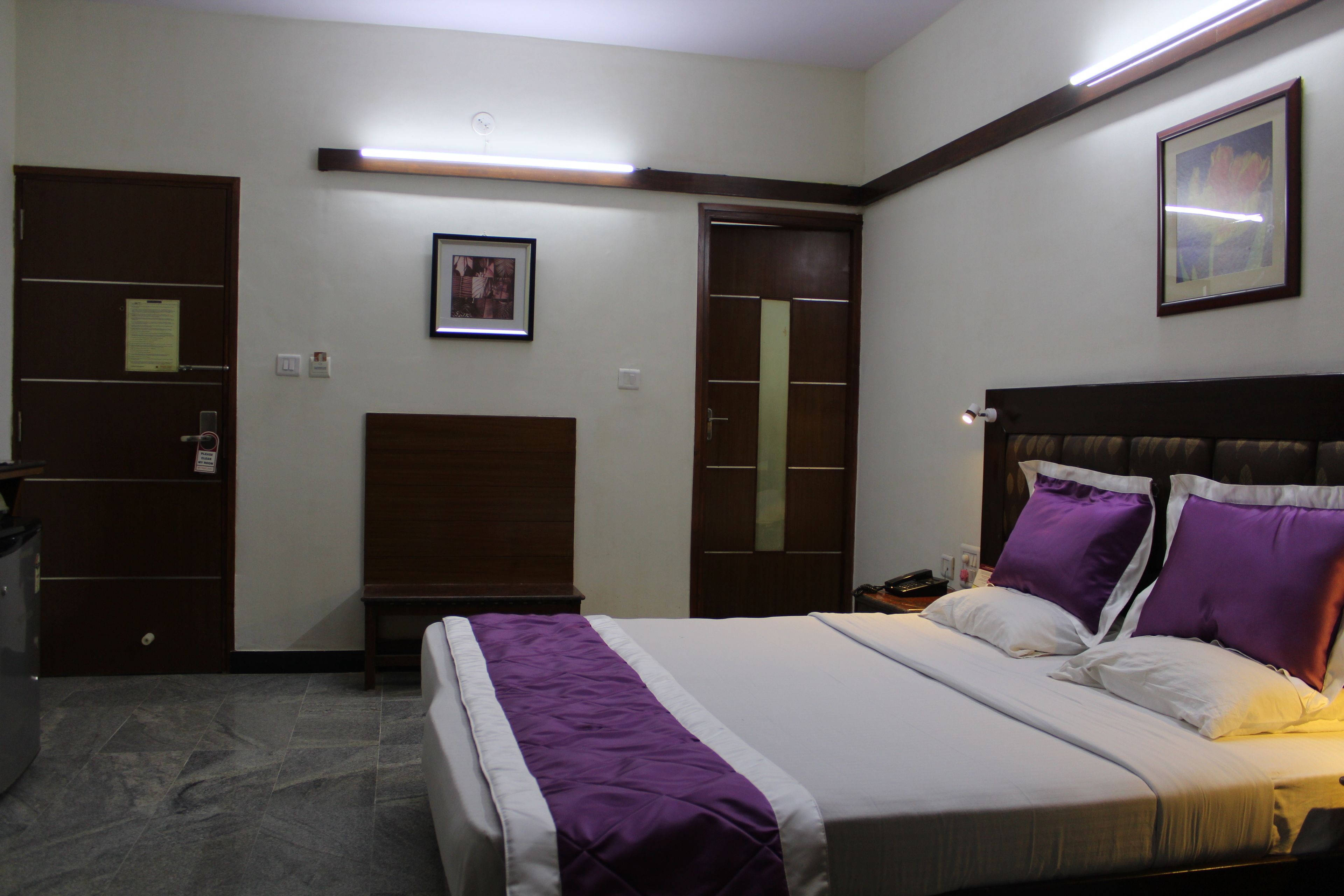 Une chambre d’hôtel avec un lit, un bureau, une chaise, une armoire et un tableau encadré au mur.